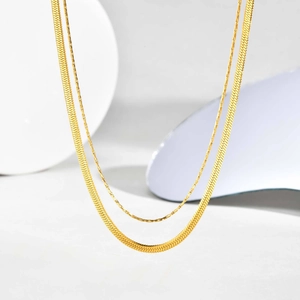 Detailed close-up of golden multi-layer necklace with flat snake chain and textured link
