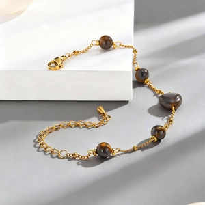 Gros plan d'un bracelet doré orné de perles d'œil de tigre brunes avec fermoir mousqueton