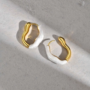 Détail macro de boucles d'oreilles vagues dorées avec émail blanc sur surface texturée