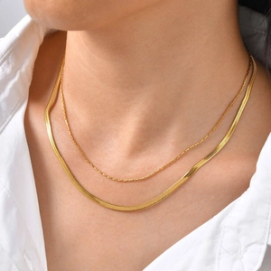 Close-up of a layered gold snake chain and dainty link necklace worn on model's neck