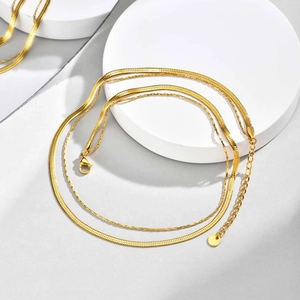 Detail of double-layered gold herringbone chain necklace with circular tag and lobster clasp