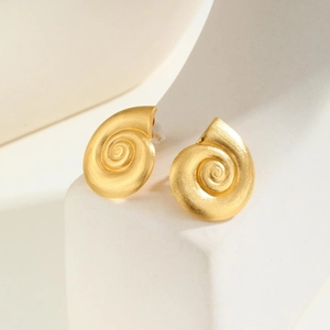 Macro shot of 18K gold spiral seashell earrings with brushed texture on a white stand