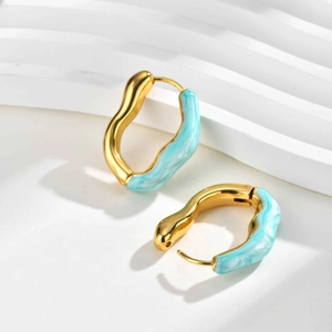 Détail macro de boucles d'oreilles vagues dorées avec incrustation émail bleu ciel