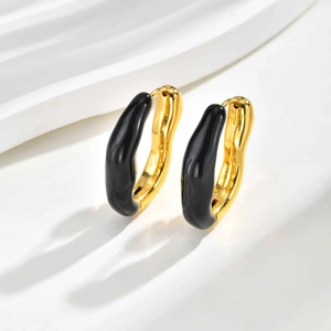 Détail de créoles dorées ondulées de luxe avec une finition noire en émail brillant