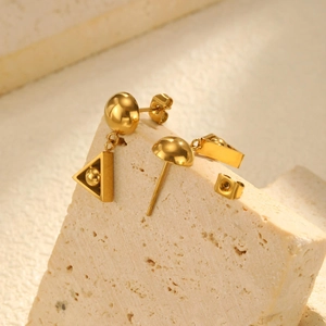Macro detail of 18K gold-plated geometric triangle earrings on a beige stone surface
