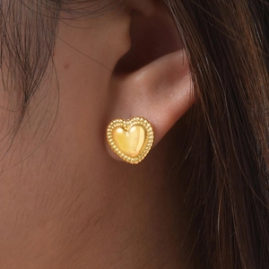 Close-up of 18K gold heart stud earrings with twisted rope texture on a model's ear