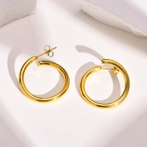 Boucles d'oreilles créoles dorées en acier inoxydable poli sur fond minimaliste chic
