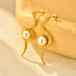 Détail de boucles d'oreilles serpent dorées avec perle blanche et texture écaillée