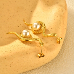 Gros plan sur des boucles d'oreilles serpent dorées avec perle et écailles