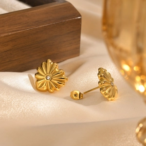 Détail de boucles d'oreilles fleur dorées avec cristal sur fond en soie beige doux