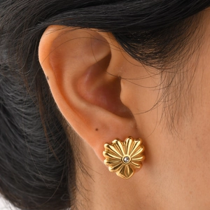 Gros plan d'une boucle d'oreille fleur dorée avec zircon central portée par mannequin