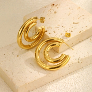 Gros plan de boucles d'oreilles doubles créoles dorées sur support en pierre beige