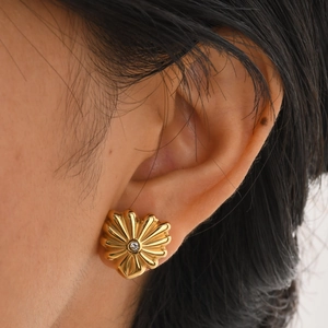 Gros plan d'un clou d'oreille fleur dorée avec zircon central porté sur l'oreille