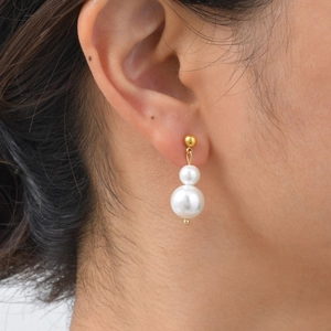 Gros plan de boucles d'oreilles dorées avec deux perles blanches verticales portées