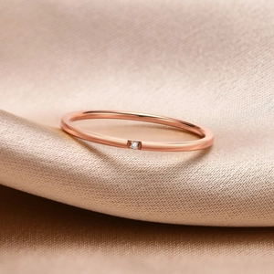 Macro shot of 1mm rose gold ring with small cubic zirconia on silk fabric