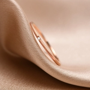 Macro detail of a thin rose gold ring with a sparkling round-cut zircon on silk background