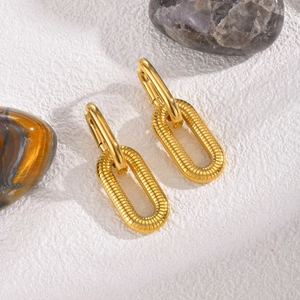 Macro detail of golden oval earrings showing textured horizontal ribbing and sleek metal finish