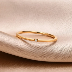 Close-up of a 1mm gold stainless steel ring with a small cubic zirconia on silk fabric