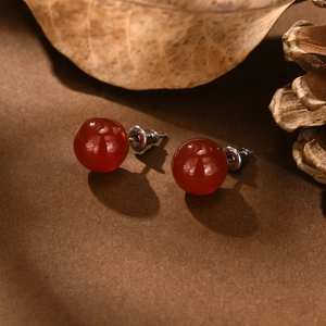 Macro detail of round red agate stud earrings with stainless steel pins on rustic background