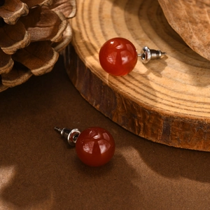 Close-up of polished red agate round stud earrings with stainless steel pins on wood
