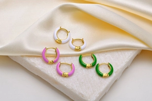 Detailed macro view of three pairs of colorful enamel gold-plated hoop earrings on marble