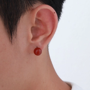 Close-up of a minimalist round red agate stud earring on ear with stainless steel pin