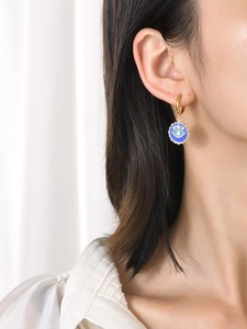 Close-up of golden stainless steel Evil Eye drop earring with blue enamel on female model