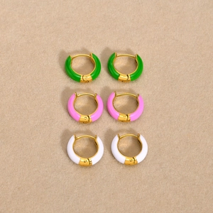 Close-up of enamel huggie earrings in green, pink, and white on textured fabric