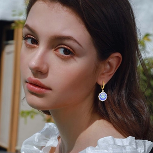 Detail shot of the golden evil eye charm earring with blue enamel and zircon worn by a model