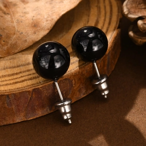 Close-up of black agate stud earrings on wood base with polished stainless steel pins