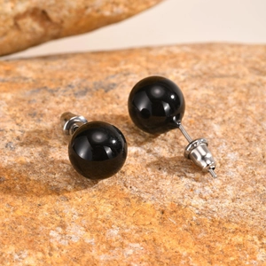 Macro shot of smooth black agate stud earrings on a natural brown textured rock background