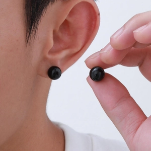 Macro view of polished black round agate stud earrings shown on ear for size
