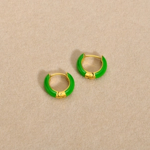 Close-up of golden hoop earring with green enamel finish on beige textured background