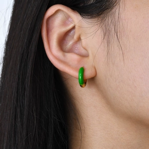 Macro shot of green enamel and gold plated huggie earring worn on a model's ear