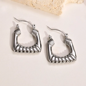 Macro detail of U-shaped silver grooved earrings on a minimalist stone background