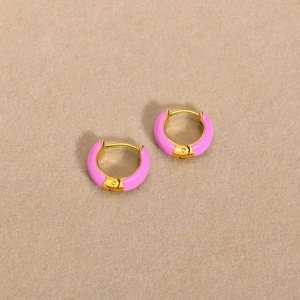 Detail view of pink enamel and gold stainless steel hoop earrings on soft beige fabric