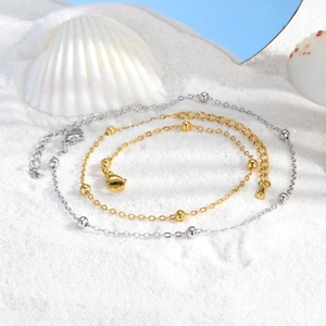 Dettaglio di cavigliere in oro e argento con perline su sabbia bianca e conchiglie marine