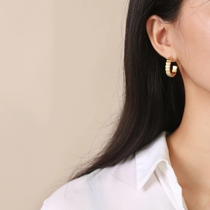 Golden C-shaped stainless steel earrings with textured rib design on female model