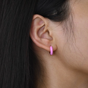 Close-up of a pink enamel hoop earring on ear with polished gold metal finish details