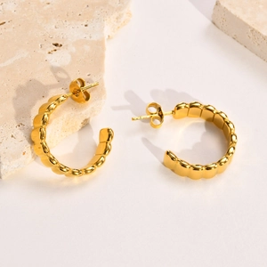 Minimalist gold C-shaped hoop earrings with wavy texture on travertine stone background