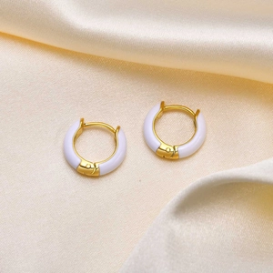 Detail of gold-plated hoop earrings with white enamel on elegant champagne silk fabric