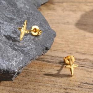 Detailed view of golden four-pointed star stud earrings on stone and wood surfaces