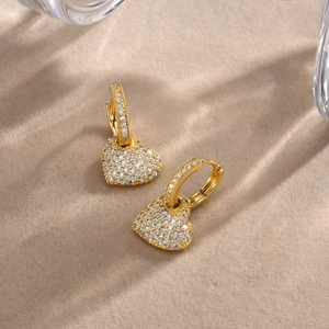Close-up of gold heart hoop earrings with sparkling cubic zirconia on beige fabric