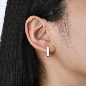 Close-up of minimalist white enamel and gold hoop earring worn on model's ear