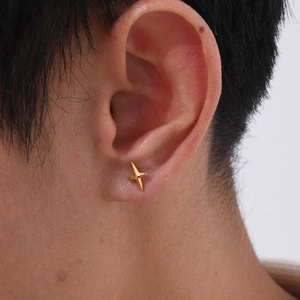 Detail of a gold four-pointed star stud earring worn by a model in a close-up shot