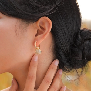 Close-up of heart-shaped gold earrings with paved cubic zirconia on a female model