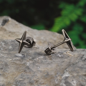 Macro shot of punk style four-pointed star earrings on a textured stone surface