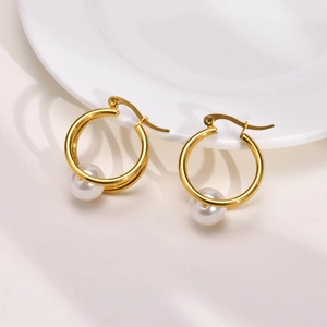 Gold hoop earrings with white pearl drop pendant on white ceramic plate background