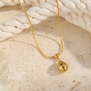 Close-up of golden egg-shaped pendant on a fine snake chain against stone and rope