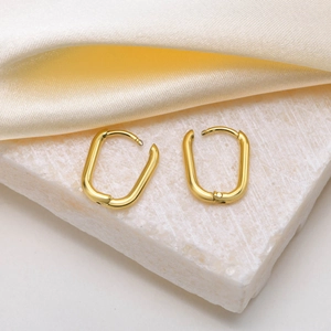 Boucles d'oreilles créoles dorées en forme de U sur pierre blanche et fond de soie